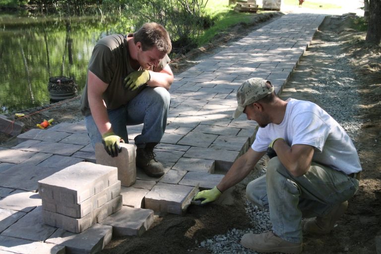 Two people laying tiles of a sidewalk