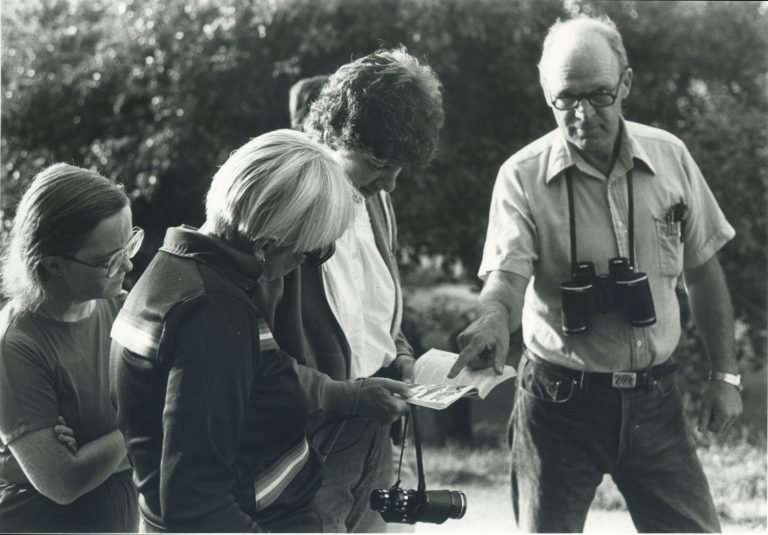 John MacArthur wearing a pair of binoculars while pointing to a piece of paper in child's hand and gazing at the camera.