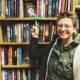 Molly Booth standing in front of bookshelves and pointing to a book