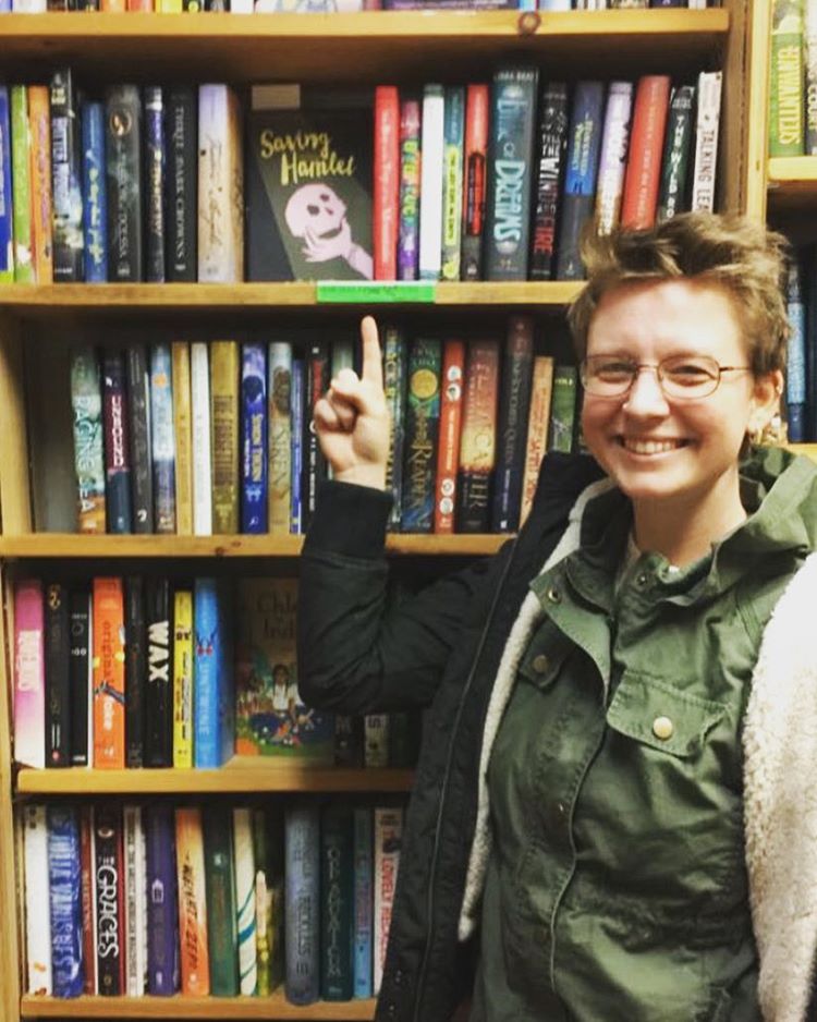 Molly Booth standing in front of bookshelves and pointing to a book