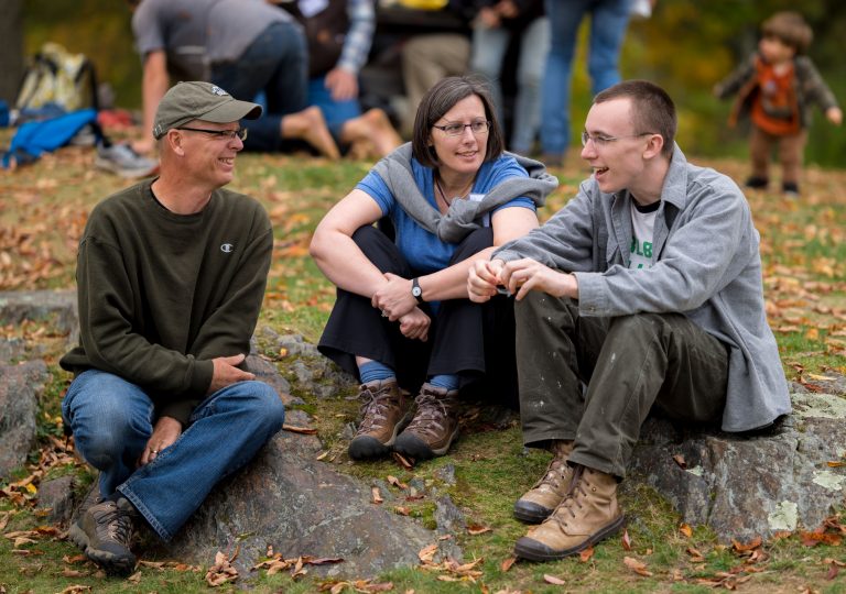 Three people sitting on grass talking with each other