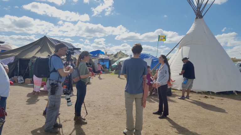 News crew filming in front of Teepees