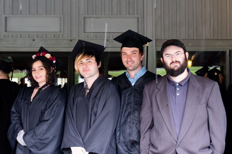 four students posing wearing their graduation caps and gowns