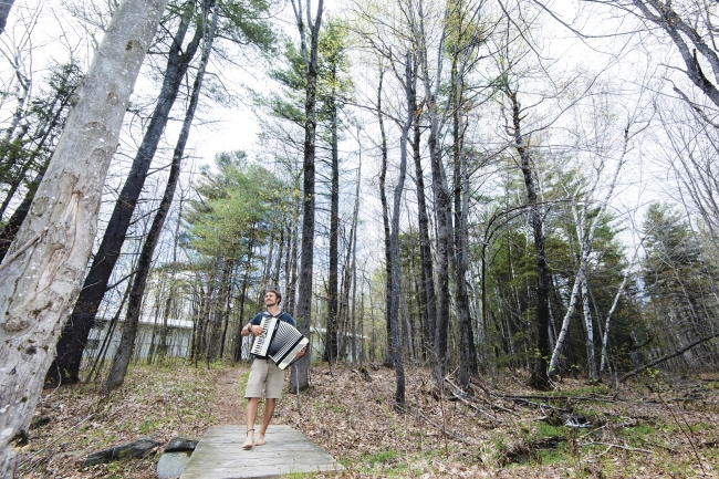 Student playing the accordion while walking through a forest path