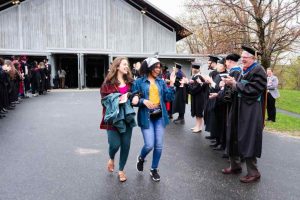 Prospective graduates walk down hill flanked by faculty