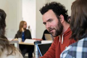 Simon sitting at a table talking with other students